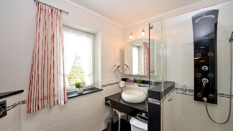 Een moderne badkamer met douche en spiegel. Helle muren en een groot raam zorgen voor een vriendelijke sfeer.