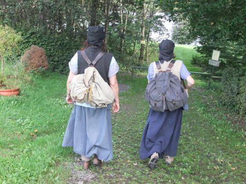 Twee vrouwen met rugzakken lopen langs een smal pad. Omringd door bomen en groen gras, lijkt de scène rustig en natuurverbonden.