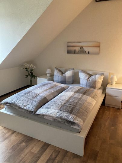 Een gezellige slaapkamer met een groot bed en gestreepte dekbedden. Naast het bed staan nachtkastjes en een plant.