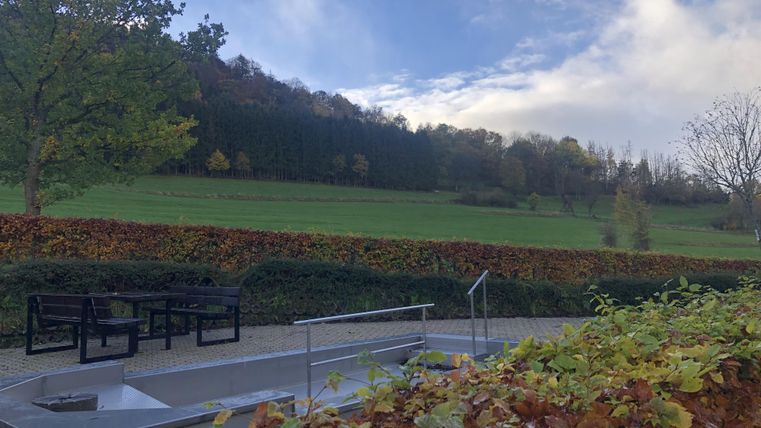 Een rustige landschap met uitzicht op groene weilanden en bomen. Op de voorgrond staan moderne zitgelegenheden op een geplaveid gebied.
