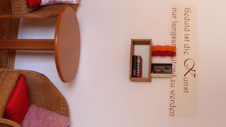 Ein gemütlicher Raum mit zwei Stühlen und einem kleinen Regal an der Wand. An der Wand steht ein inspirierender Spruch.