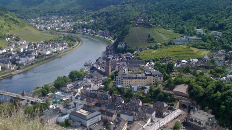 Een schilderachtig stadje aan de rivier met groene heuvels op de achtergrond. De architectuur bestaat uit traditionele gebouwen die harmonieus in het landschap passen.