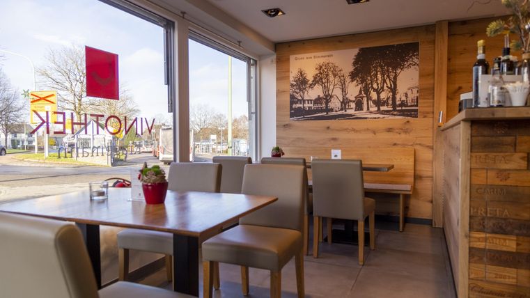 Een gezellig café met houten meubels en grote ramen. Door de ramen is een fijne lichtsfeer te zien.