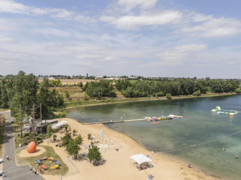 A beautiful beach with fine sand and green water. In the background, trees and recreational activities can be seen.