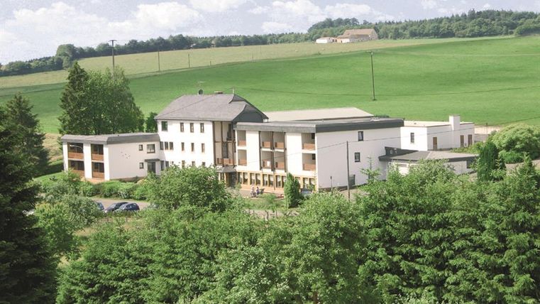 A modern building surrounded by trees and meadows. The sky is clear and the landscape looks peaceful.