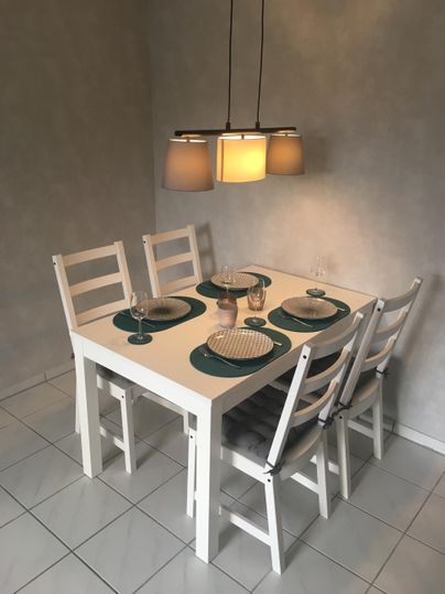 A bright dining room with a white table and four chairs. The table is nicely set and is illuminated by a modern pendant light.