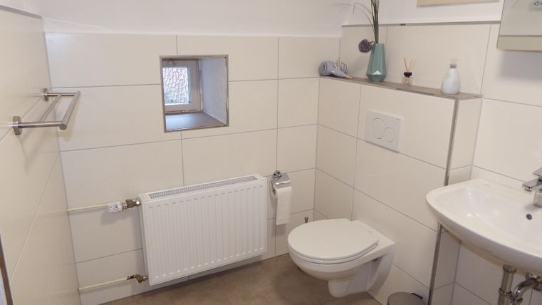 A small, modern bathroom with bright tiles. It contains a sink, a toilet, and a radiator.