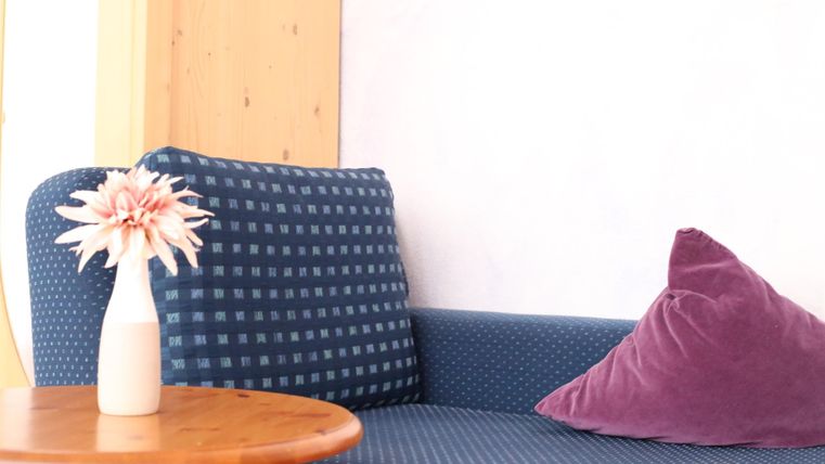 Eine blaue Couch mit einem lila Kissen und einem kleinen Tisch. Auf dem Tisch steht eine Vase mit einer Blume.