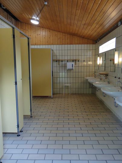 Ein heller, geräumiger Badezimmerbereich mit drei Waschbecken und Trennwänden. Der Boden ist gefliest, und die Decke ist aus Holz.