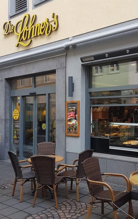 Einladendes Café mit gemütlichen Sitzplätzen im Freien. Die Schaufenster zeigen eine Auswahl an Backwaren und Snacks.