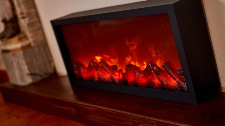 A modern electric fireplace with flickering flames and logs. The fireplace gives the room a cozy atmosphere.