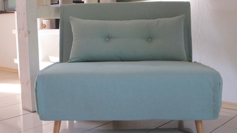 Ein modernes, mintgrünes Sofa mit einem Kissen. Der Boden ist hell und die Wände sind in neutralen Farben gehalten.
