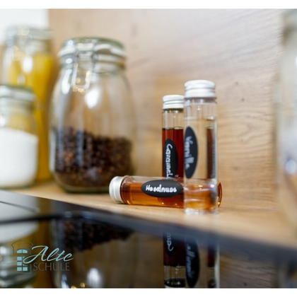 Ein stilvoller Küchentresen mit verschiedenen Gläsern und kleinen Flaschen. Die Flaschen enthalten Liköre oder Essenzen, beschriftet mit handgeschriebenen Etiketten.