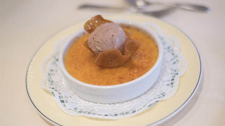 Een heerlijke crème brûlée met een bolletje chocolade-ijs en een krokant wafelblaadje. Het dessert is opgediend in een witte kom op een verfijnde schotel.