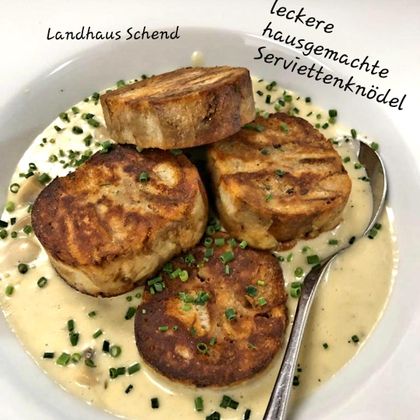 Ein Teller mit leckeren, hausgemachten Serviettenknödeln, angerichtet mit einer cremigen Sauce. Gehackter Schnittlauch verleiht dem Gericht eine frische Note.