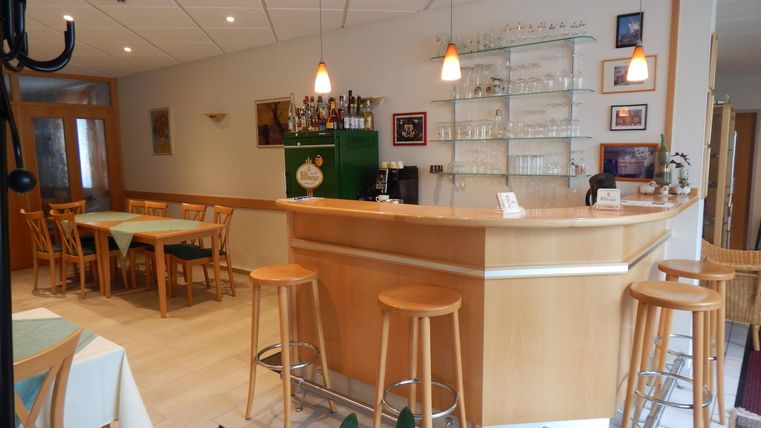 An inviting bar with a wooden counter and modern bar stools. The room is brightly lit and has a cozy atmosphere.