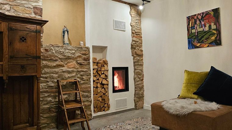 A cozy living room with a modern fireplace and colorful flooring. There is a wooden cabinet, a comfortable couch, and a stylish chandelier.