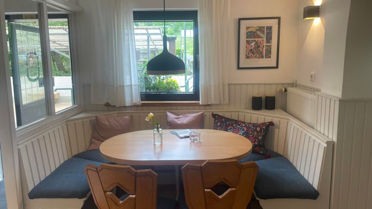 Een gezellige eetruimte met een ronde tafel en zitplaatsen. Grote ramen laten veel daglicht de ruimte binnen.