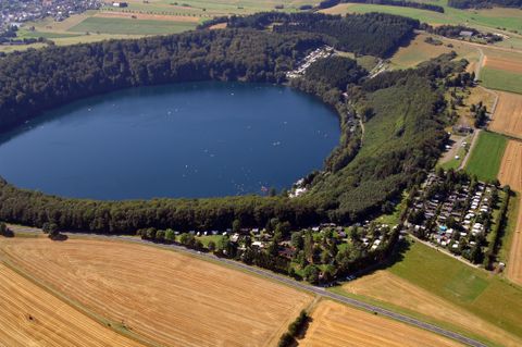 Een grote, ronde meer is omringd door groene bossen. In de buurt zijn er campings en veel open landschap.