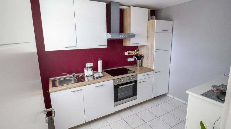 A modern kitchen with white cabinets and a red wall. It is well-equipped with a stove, oven, and sink.