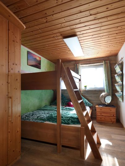 A cozy bedroom with a wooden loft bed. The walls are painted green and the room has plenty of natural light.