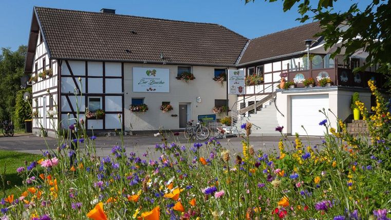 A charming half-timbered house with colorful flowers in the foreground. The sky is clear and the surroundings are inviting.
