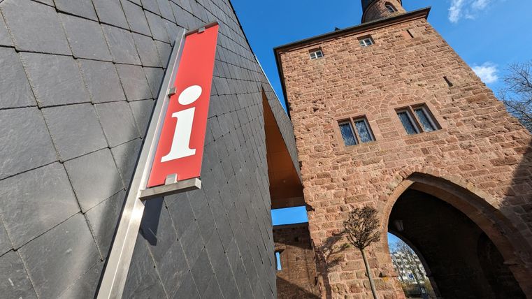 Ein Informationsschild steht vor einem alten Steinturm. Der Himmel ist blau und die Architektur ist gut sichtbar.