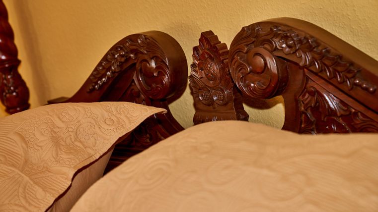 An intricately carved wooden headboard with elegant details. Two light cushions are placed on a bed.