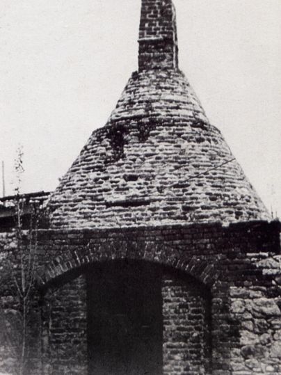 A historic, brick building with a conical roof. The structure shows signs of wear and is surrounded by an old wall.
