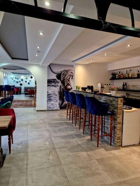 Een modern restaurant met een stijlvolle bar en comfortabele blauwe zitplaatsen. Op de achtergrond is een indrukwekkende wanddecoratie met een leeuw te zien.