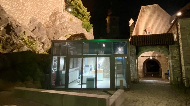 Ein moderner Glasanbau in einer historischen Burgumgebung bei Nacht. Die Umgebung ist von alten Steinmauern und einem sanften Licht beleuchtet.