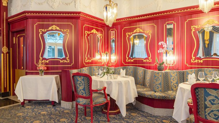 Een elegant restaurant met rode wandverf en stijlvolle spiegels. Gezellige tafels en een smaakvolle ambiance nodigen uit om te blijven hangen.