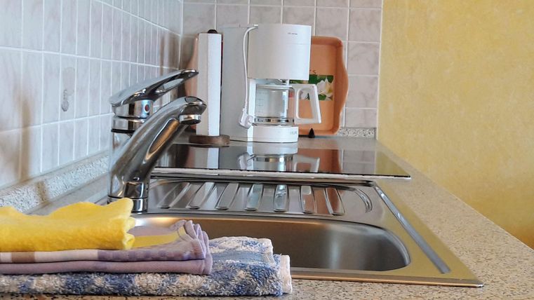 Een moderne keuken met een gootsteen en een koffiezetapparaat. Op het aanrecht liggen theedoeken.