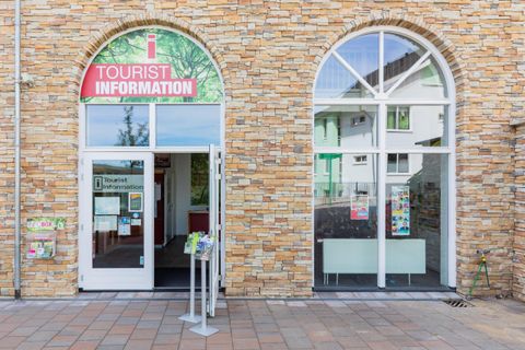 Een toeristeninformatiecetrum met een uitnodigende ingang. De façade is gemaakt van lichte steen en het bord wijst op toeristische informatie.