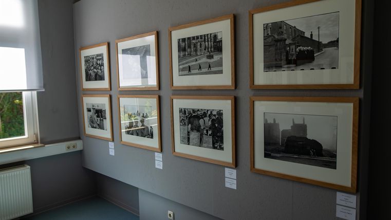A gallery with black-and-white photographs in framed images. The pictures display various historical scenes on a wall.