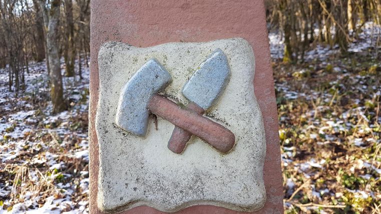 Ein Schild mit einem Symbol von Hammer und Spitzhacke. Es steht in einem Waldgebiet mit leicht verschneitem Fußboden.