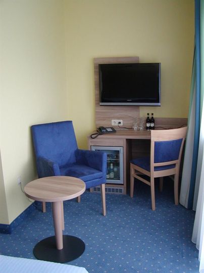 Een gezellige hotelkamer met een televisie, een kleine tafel en twee stoelen. Er is ook een koelkast en een telefoonaansluiting.