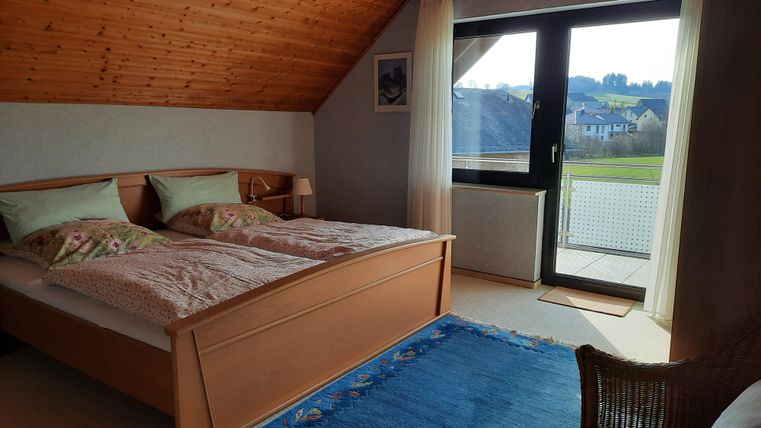 A cozy bedroom with a double bed and soft colors. Large windows provide a view of the surroundings.