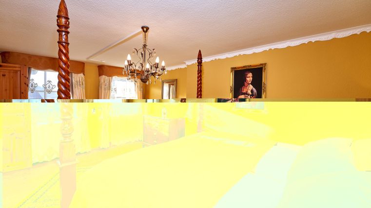 A cozy room with a chandelier and wooden columns. A portrait hangs on the wall.