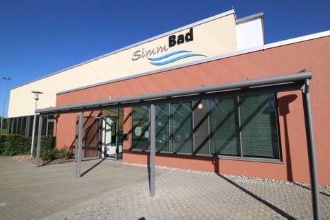 Ein modernes Gebäude mit der Aufschrift "Simun Bad". Die Fassade ist hell und verfügt über große Fenster.