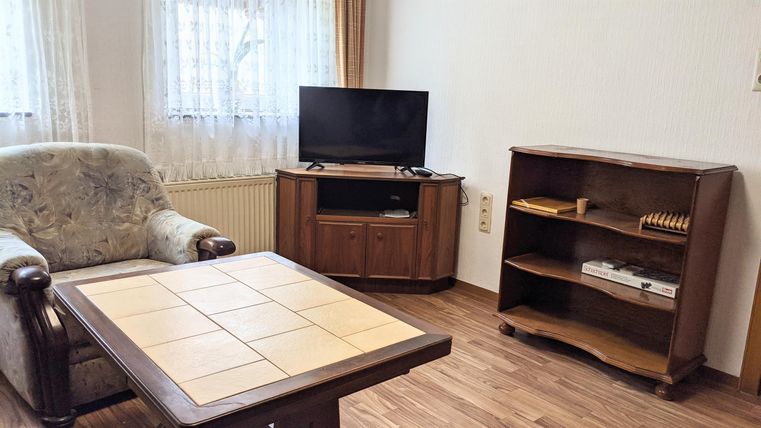 A cozy living room with a TV, a table, and a wooden shelf. The decor feels inviting and friendly.
