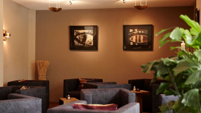 A cozy room with blue sofas and elegant wall art. In the foreground, a green plant creates a relaxed atmosphere.