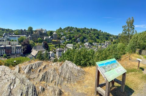 A view of a picturesque town with green hills in the background. In the foreground, there is an information board on a rock.