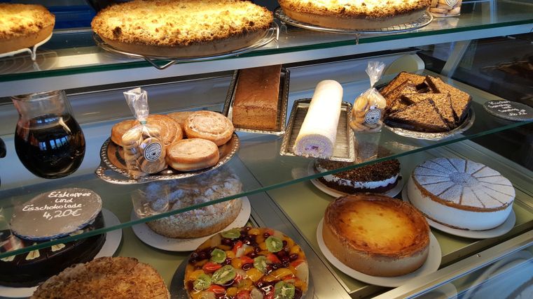 Eine Auslage mit verschiedenen Kuchen und Süßigkeiten. Die Auswahl umfasst Torten, Plätzchen und Obstkuchen.