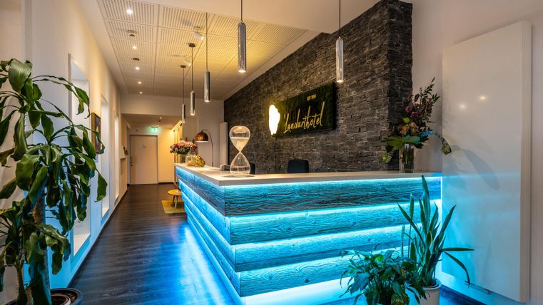 A modern reception area with an elegant, illuminated reception desk. In the background, plants and a stylish wall design can be seen.