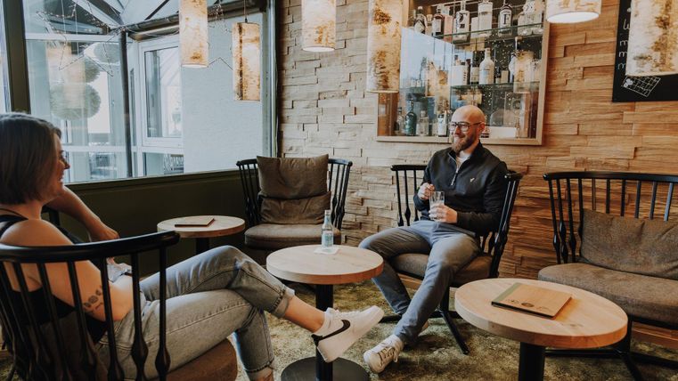 Zwei Personen sitzen entspannt in einem gemütlichen Ginothek. Die Einrichtung ist modern mit Holz- und Lichtelementen.