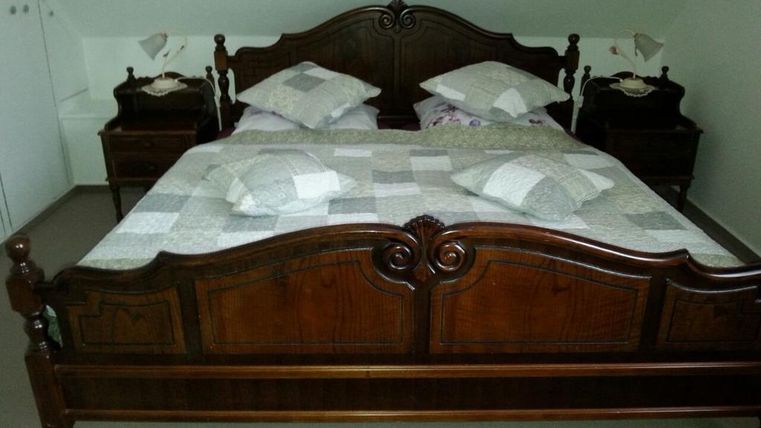 Ein rustikales Schlafzimmer mit einem großen Holzbett und gestreiften Kissen. Neben dem Bett stehen zwei Nachttische.