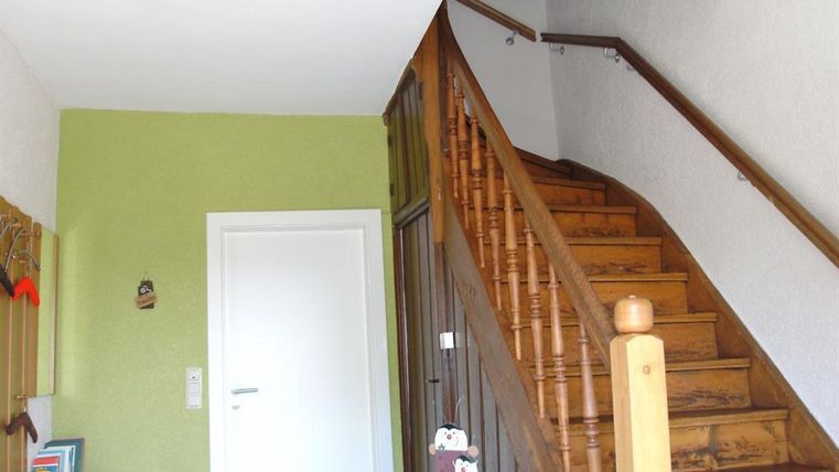 Ein heller Eingangsbereich mit einer Holztreppe. Die Wände sind teilweise grün gestrichen und es gibt einen kleinen Ablagetisch.