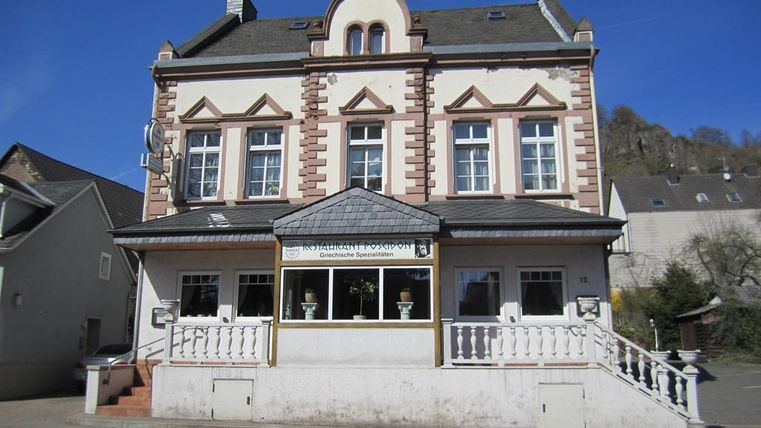 Two-story building with a classic facade, sign 'Restaurant Poseidon', Greek specialties. Staircase and railing in the foreground.