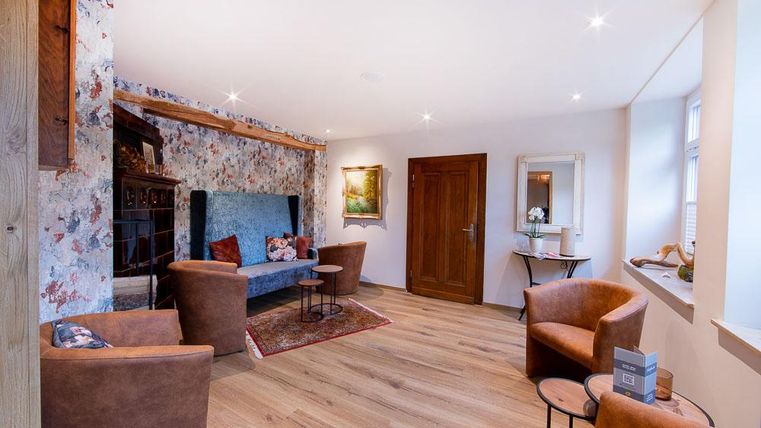 Ein gemütliches Wohnzimmer mit einem blauen Sofa und mehreren braunen Sesseln. Die Wände sind mit floralem Muster dekoriert und der Boden ist aus Holz.